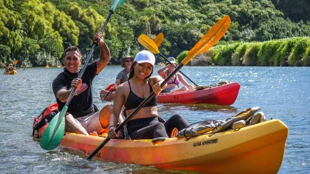 Smiling couple paddling a yellow kayak on the Wailua River with Kayak Adventures Kauai, enjoying scenic views and tropical sunshine.