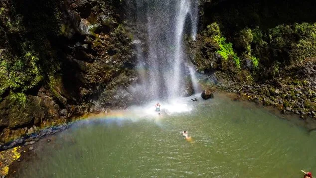 Swimmers cooling off beneath a cascading waterfall surrounded by lush cliffs near Wailua River, an adventurous stop with Kayak Adventures Kauai.