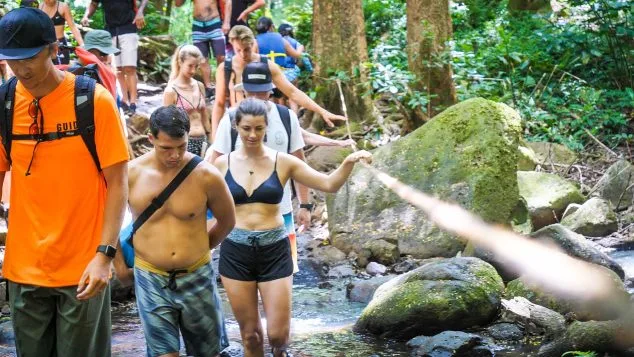 Group hiking through a lush jungle trail using a rope assist during a guided Kayak Adventures Kauai waterfall and kayak tour.