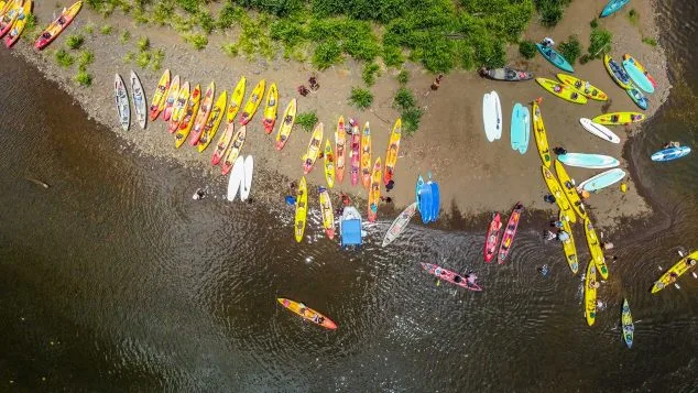 Aerial view of vibrant kayaks lined up along the sandy shoreline for Kayak Adventures Kauai river tours.